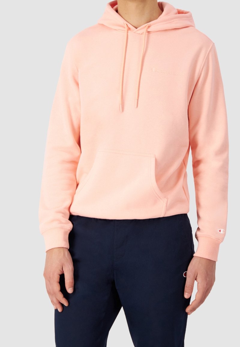 Felpa rosa chiaro con tasca frontale, cappuccio regolabile e logo ricamato sul petto, abbinata a pantaloni blu scuro.