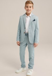 Hele sinine ülikond kohandatud jakk ja nöörpüksid. Valge nööpidega särgiga ja tumesinine taskuvaru. Kandmine valgete sneakerite kõrval.