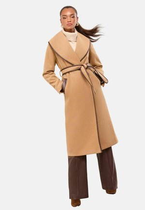 Palton dintr-un amestec de lână cămilă, cu un guler lat, accente din piele maro, curea legată și buzunare laterale, asortat cu pantaloni largi maro.