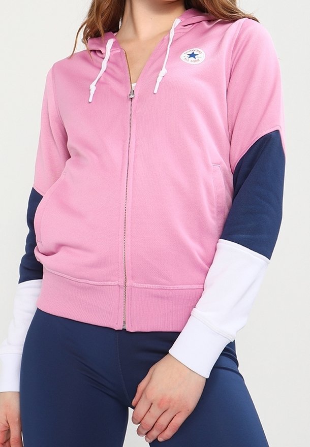 Felpa rosa con cerniera e accenti blu e bianchi, dotata di cappuccio, cordini bianchi e un logo tondo sul petto. Tessuto dalla consistenza liscia.