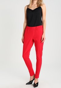 Pantalons rouges fuselés avec une taille élastique, associés à un débardeur noir et des chaussures à talons hauts vernies noires. Texture de tissu lisse.