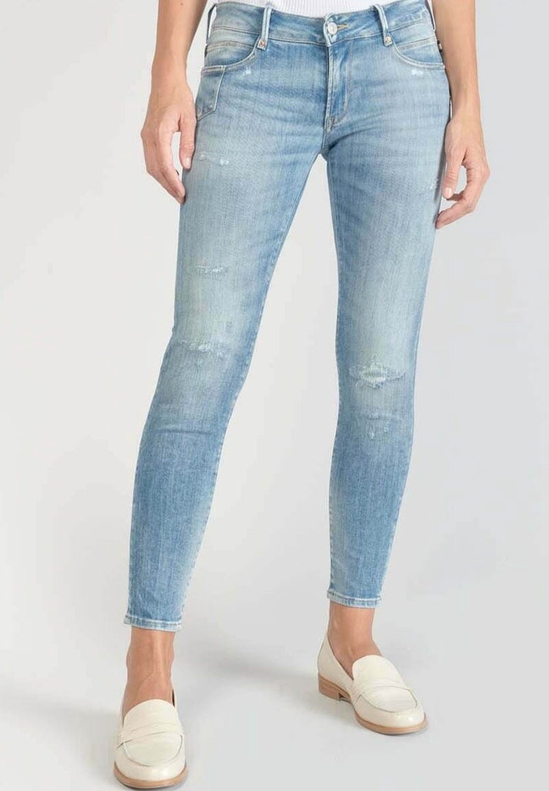 Vaqueros ajustados de mezclilla azul claro con lavado descolorido. Presentan detalles desgastados y diseño de cinco bolsillos. Combinados con mocasines blancos.