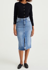 Svart långärmad kavaj med guldknappar, kombinerad med en blå jeanskjol i blyertsstil med en framdekal och klassisk passform. Svarta loafers fulländar outfiten.