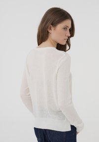 Maglione bianco leggero e trasparente con scollatura rotonda e orlo a coste. Presenta maniche lunghe e una vestibilità rilassata.