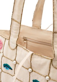 Torebka tote wykonana z kremowego materiału, ozdobiona kolorowymi haftowanymi oczami, sztucznymi perłami i złotymi akcentami. Zawiera wewnętrzną kieszeń na zamek.
