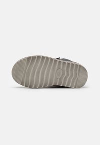 Graue Schuhsohle mit einem strukturierten Muster und Rillen für besseren Halt, aus Gummimaterial gefertigt, mit abgerundeten Kanten und flachem Profil.