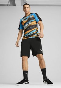 Puma spordisärk sinises, oranžis ja mustas värvitoonis lainelise mustriga; koos mustade lühikeste pükste ja mustade tossudega, millel on valged aktsendid.