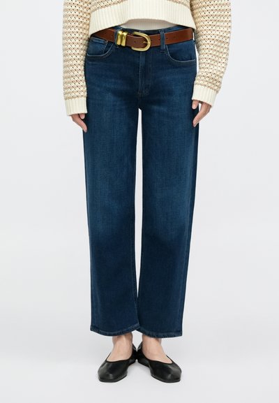 Jeans azul de perna larga feitos de ganga, com bolsos frontais, passadores para cinto e um cinto de pele castanha com fivela dourada.