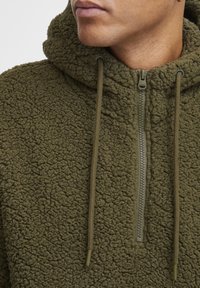 Olive green hoodie made from textured fleece, featuring a half-zip closure and drawstrings for the hood. Soft, warm fabric.