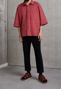 Košile s krátkým rukávem na knoflíky v barvě prachové růže, s jednou náprsní kapsou. Kombinováno s černými manšestrovými kalhotami a masivními černými sandály.