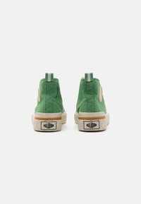 Sneakers alte in tela verde con suole in gomma bianca, dotati di un accento con logo rotondo sul lato e due linguette verticali a striscia.