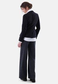 Schwarzer Cordblazer mit weißem Kragen, kombiniert mit grauen weit geschnittenen Hosen, die ein elegantes, maßgeschneidertes Design und strukturierten Stoff präsentieren.