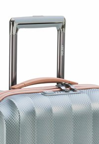 Valigia rigida blu con un motivo a diamante testurizzato, ruote doppie, maniglia in oro rosa, chiusura a zip e lucchetto TSA. Marca: Delsey.