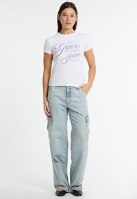 Valge lühikeste varrukatega T-särk sinise tekstiga, mis ütleb "Guess California Jeans." Kombineeritud helesiniste kaanepükstega, millel on küljetaskud.