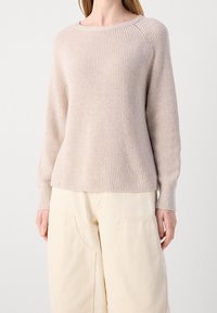 Pull en maille beige clair avec une texture côtelée, col rond et manches longues, porté sur un pantalon large crème.