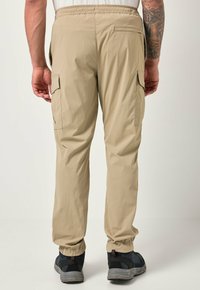 Pantaloni cargo beige con vita elastica, tasche laterali, e polsini elastici alle caviglie, abbinati a calzature scure.
