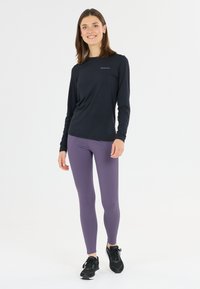 Svart långärmad tröja och lila leggings i stretchtyg, med en tajt design och en diskret logotyp på tröjan. Svarta träningsskor.
