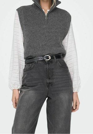 Femme portant un gilet en maille gris sans manches sur un chemisier blanc à manches longues, associé à un jean noir délavé taille haute et une ceinture noire.