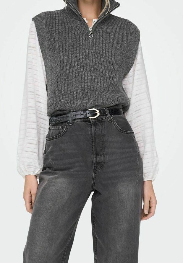 Femme portant un gilet en maille gris sans manches sur un chemisier blanc à manches longues, associé à un jean noir délavé taille haute et une ceinture noire.