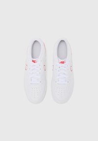 Hvide sneakers med en glat læderstruktur, snørebåndsdesign, perforeret tå og røde Nike swoosh-accenter på siderne og tungen.