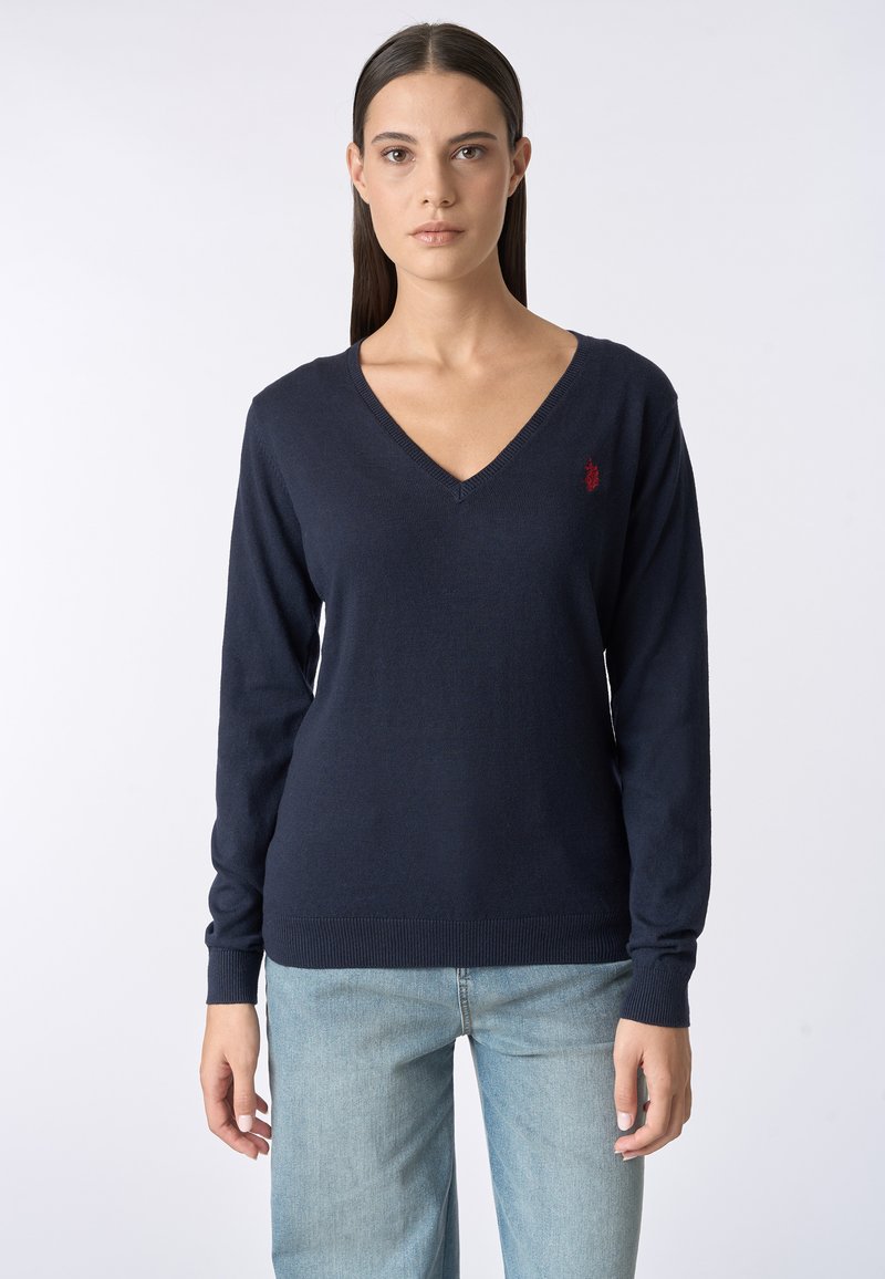 Maglione a V navy in morbido tessuto con maniche lunghe. Presenta un piccolo logo rosso sul lato sinistro del petto e bordi e polsini a coste.