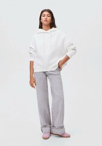 Felpa bianca con cappuccio, taglio oversize; jeans grigi a gamba larga con risvolti; scarpe rosa. Design semplice; texture morbida; nessun motivo o accessorio visibile.