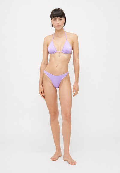 Lillā bikini, kuram ir trīsstūra forma ar rufflēm malās un zvaigznītes piekariņu, kopā ar saskaņotiem zemas piegriezuma dibentiem. Gluda tekstūra.