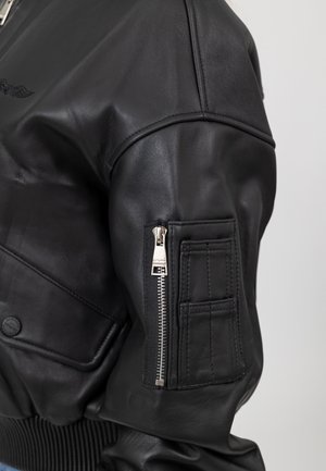 Zwarte leren bomberjack met ribgebreide manchetten, een ritszak op de mouw en een gladde textuur met een subtiele glans.