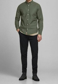 Olive green button-down shirt with long sleeves and a chest pocket, paired with black pinstriped pants and dark footwear.