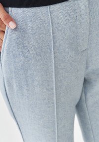Lichtblauwe herringbone patroon broeken met verticale streepjes. Gemaakt van geweven stof. Zijkant zakdetails zichtbaar.