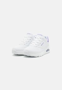 Zapatillas Skechers en blanco con acentos morados. Cuentan con paneles de malla, suela de goma gruesa y plantilla acolchada para mayor comodidad.