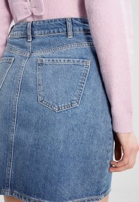 Denimkjol i ljusblått, med medelhög midja, bakfickor, fransad fåll och en subtil textur, parat med en mjuk rosa tröja.