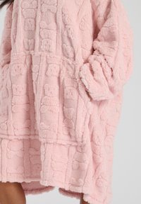 Piumino rosa con cappuccio fatto di un morbido tessuto peluche con un motivo testurizzato. Presenta maniche larghe e una tasca a marsupio.