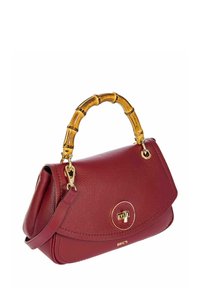 Sac à main en cuir rouge avec une anse en bambou incurvée, des accessoires en or et une fermeture à rabat arrondi mettant en avant un détail en forme de logo circulaire.