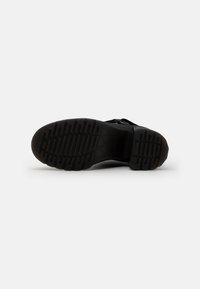 Semelle de chaussure noire en caoutchouc texturé pour une meilleure traction, présentant un motif de semelle et un design de bout rond.