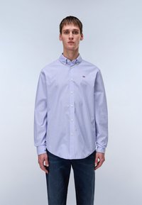 Light purple long-sleeve shirt with a button-down collar, featuring white buttons and a small logo detail on the left chest. Worn with dark jeans.
