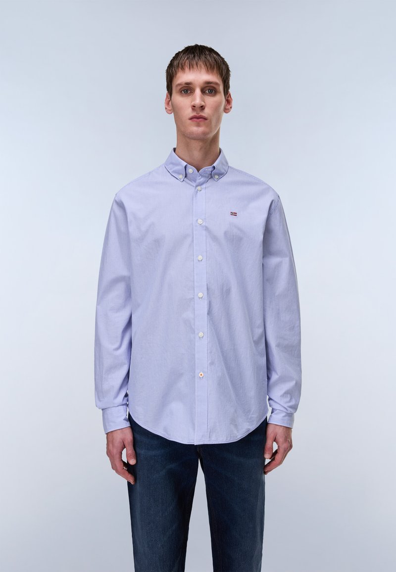 Light purple long-sleeve shirt with a button-down collar, featuring white buttons and a small logo detail on the left chest. Worn with dark jeans.
