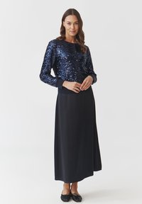 Jūras spēku gaiši zils sequined kardigāns ar apaļu kakla izgriezumu un pogu aizdari, kombinēts ar garu, vienkrāsainu melnu svārku. Gluda tekstūra un pieguļoši piedurknes.