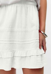 Falda blanca de volantes con un tejido texturizado, que presenta un dobladillo con volantes y un borde decorativo de encaje. Cintura elástica y un acabado suave.