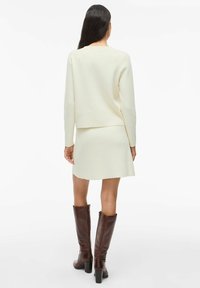 Ensemble de pull crème et jupe assortie en tissu tricot doux, associé à des bottes en cuir marron montantes avec un talon carré.