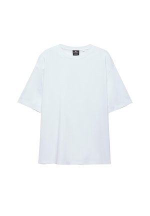 Hvid, oversized T-shirt med korte ærmer og rund halsudskæring, med en sort etiket inde i kraven på en hvid baggrund.
