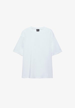Hvid, oversized T-shirt med korte ærmer og rund halsudskæring, med en sort etiket inde i kraven på en hvid baggrund.