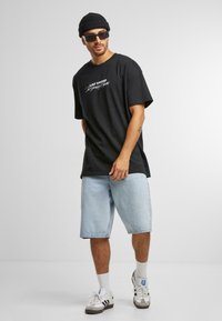 Sort t-shirt med korte ærmer med "Las Vegas" grafik, parret med lyseblå denimshorts og grå sneakers med hvide detaljer og sokker.