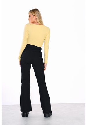 Top a maniche lunghe in maglia a coste gialla chiara, abbinato a pantaloni neri a vita alta e svasati. Stivali platform neri completano l'outfit.