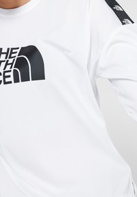 Vitt långärmad skjorta med stort svart "The North Face"-tryck på bröstet och mindre logotyper på höger ärm.