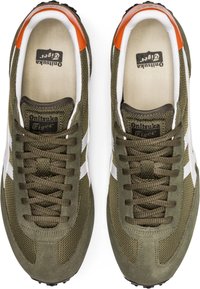 Baskets en daim vert et mesh avec accents blancs, bout rond, surface texturée, et détail orange au talon. Lacets et semelle intérieure de marque visibles.