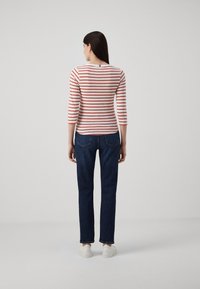 Camicia a righe rosse e bianche con maniche a tre quarti, jeans blu e sneakers bianche. La camicia ha un collo rotondo e un design aderente.