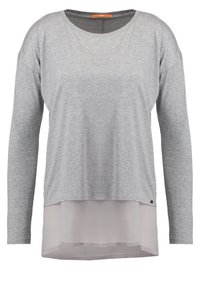 Vaaleanharmaa pitkähihainen kerrospaita, jossa pehmeä ohut valkoinen kangas ulottuu helman alapuolelle.