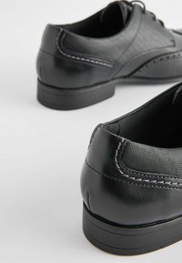 Czarne skórzane buty z teksturowanym panelem materiałowym, kontrastowym szwem i niskim obcasem. Okrągły czubek i sznurowany fason.
