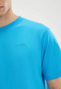 Camiseta de algodón de manga corta azul con cuello redondo acanalado y sutil bordado del logo en el pecho. Textura suave y corte holgado.